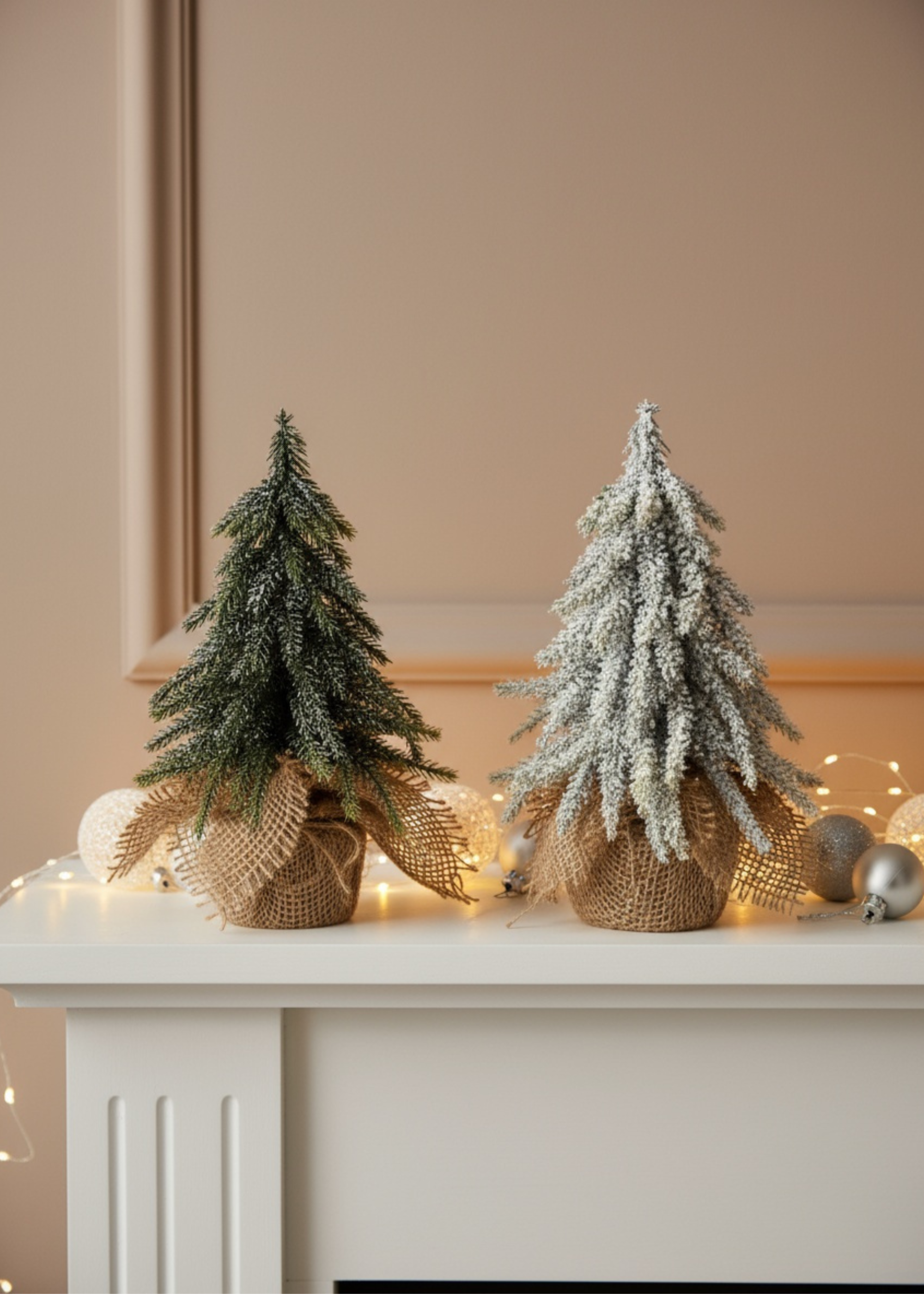 Truly Lifestyle Two small Christmas trees on a mantelpiece with decorative ribbons and lights.