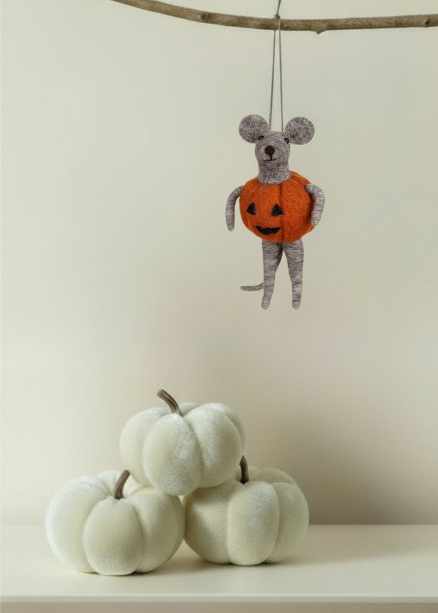 Decorative mouse in an orange pumpkin costume hanging above white pumpkins on a neutral background