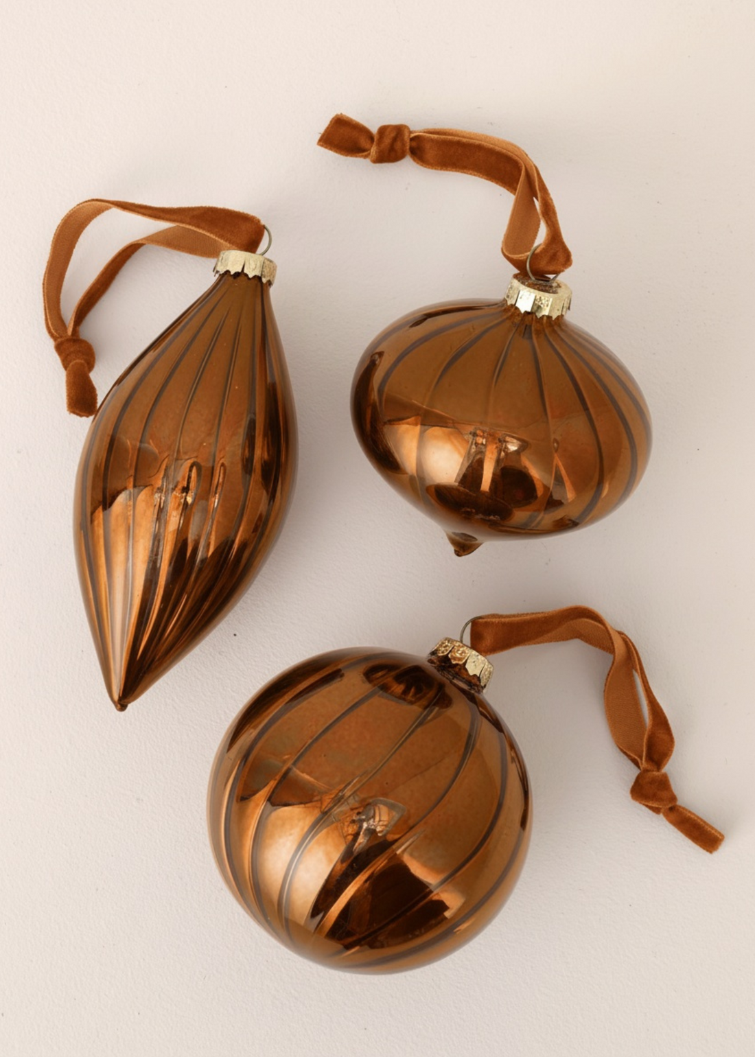 Three brown glass ornaments with ribbed texture on a beige background