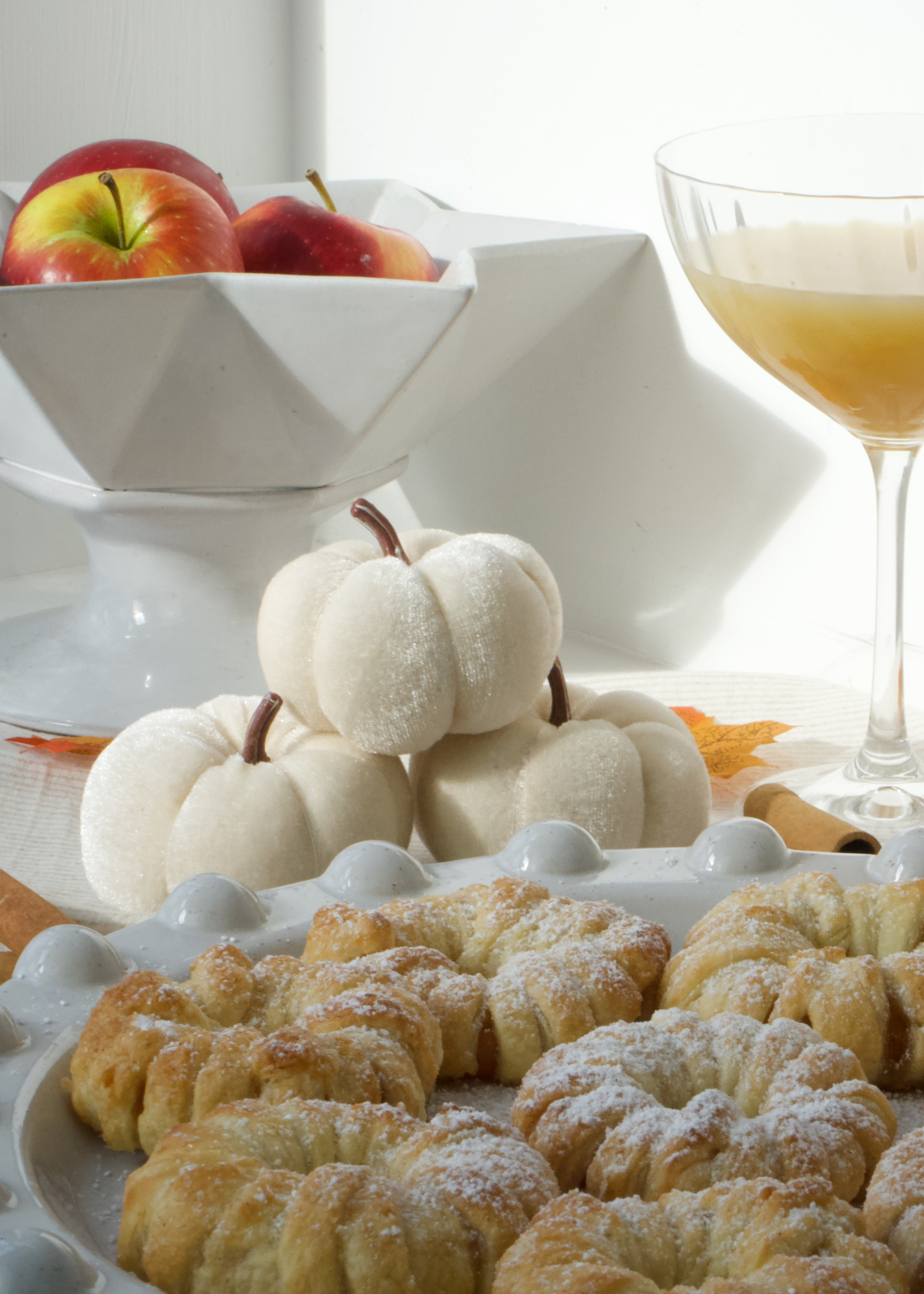 Decorative white pumpkins with pastries on a table setting with apples and a glass of orange juice by Truly Lifestyle.