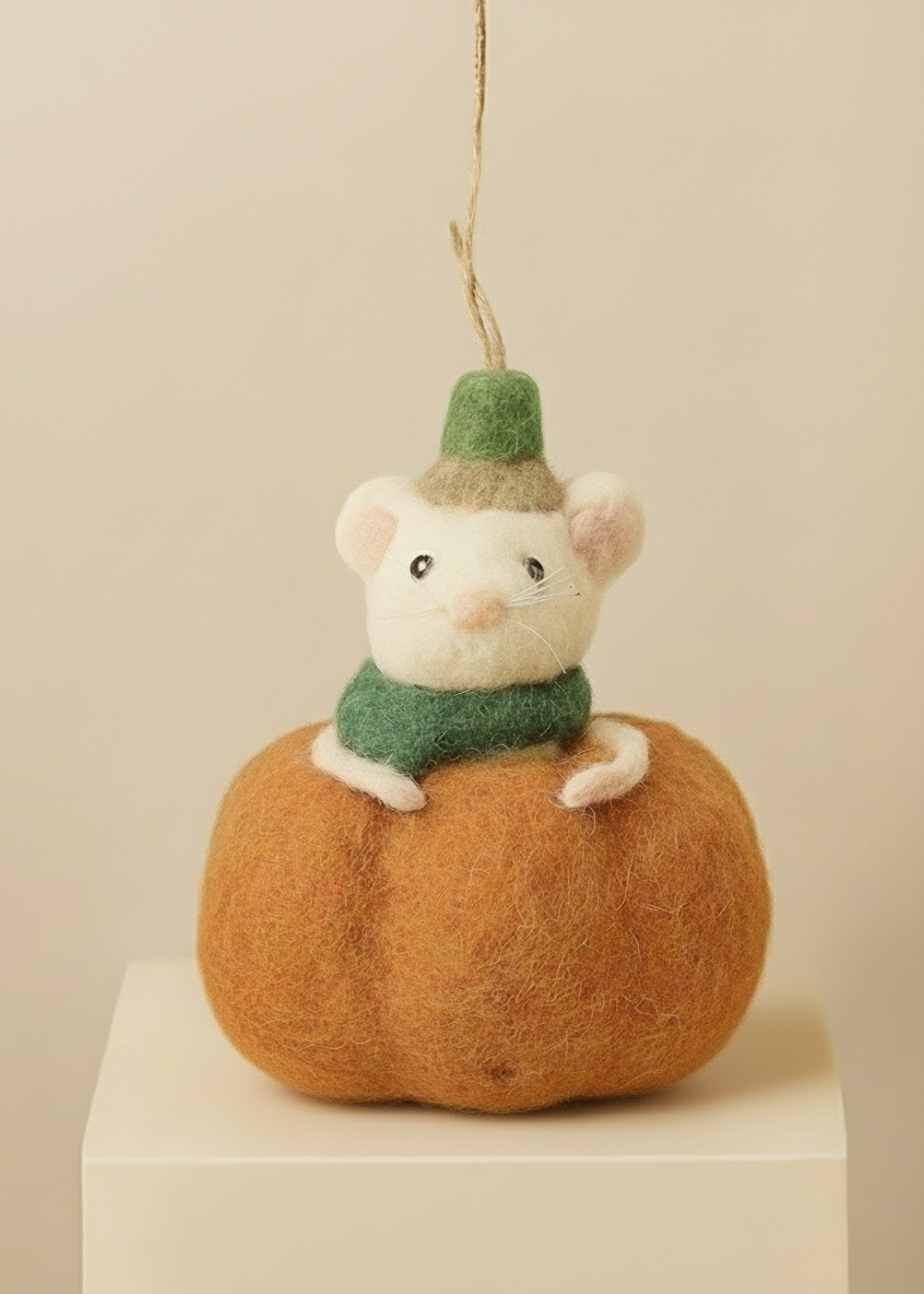 Stuffed mouse in a green hat and scarf sitting on a felt pumpkin against a beige background Truly Lifestyle