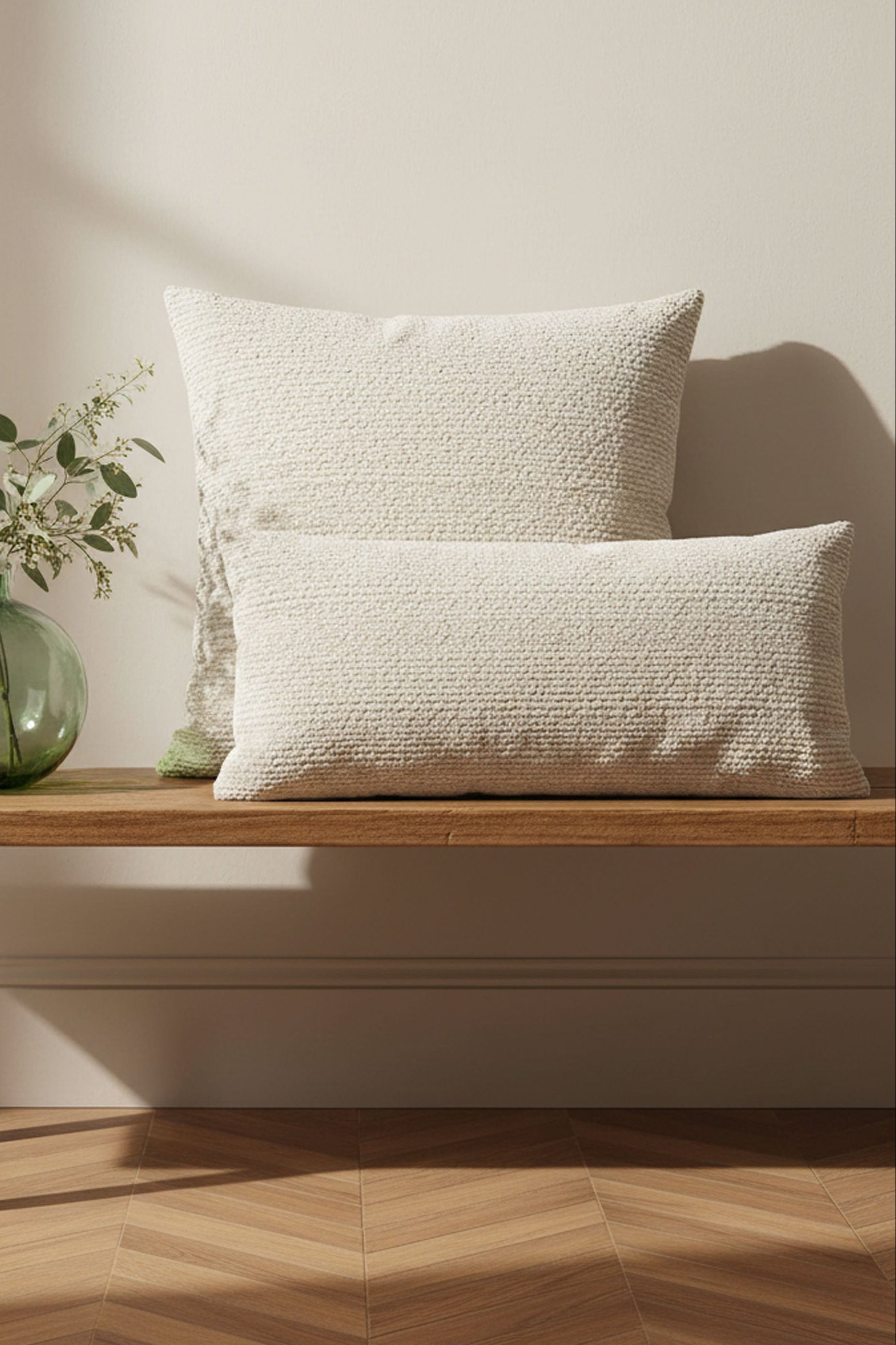 Two textured pillows on a wooden bench with a vase of flowers in the background.
