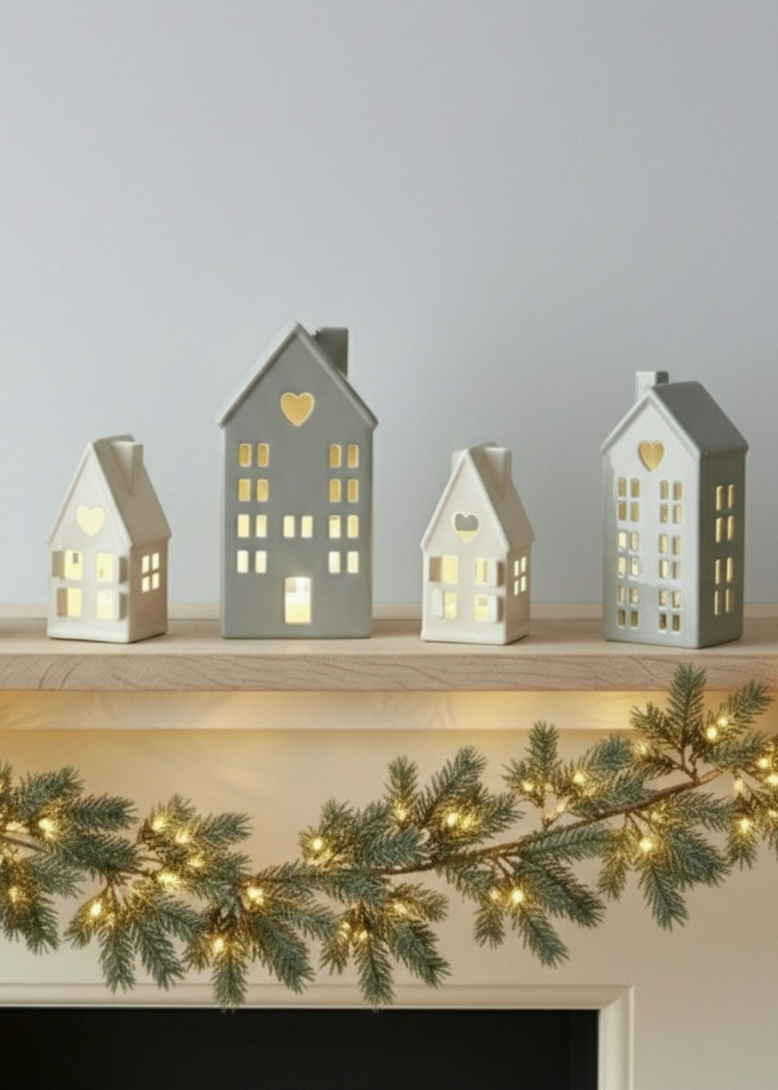 Truly Lifestyle Set of small house-shaped lanterns on a mantelpiece with a Christmas garland.
