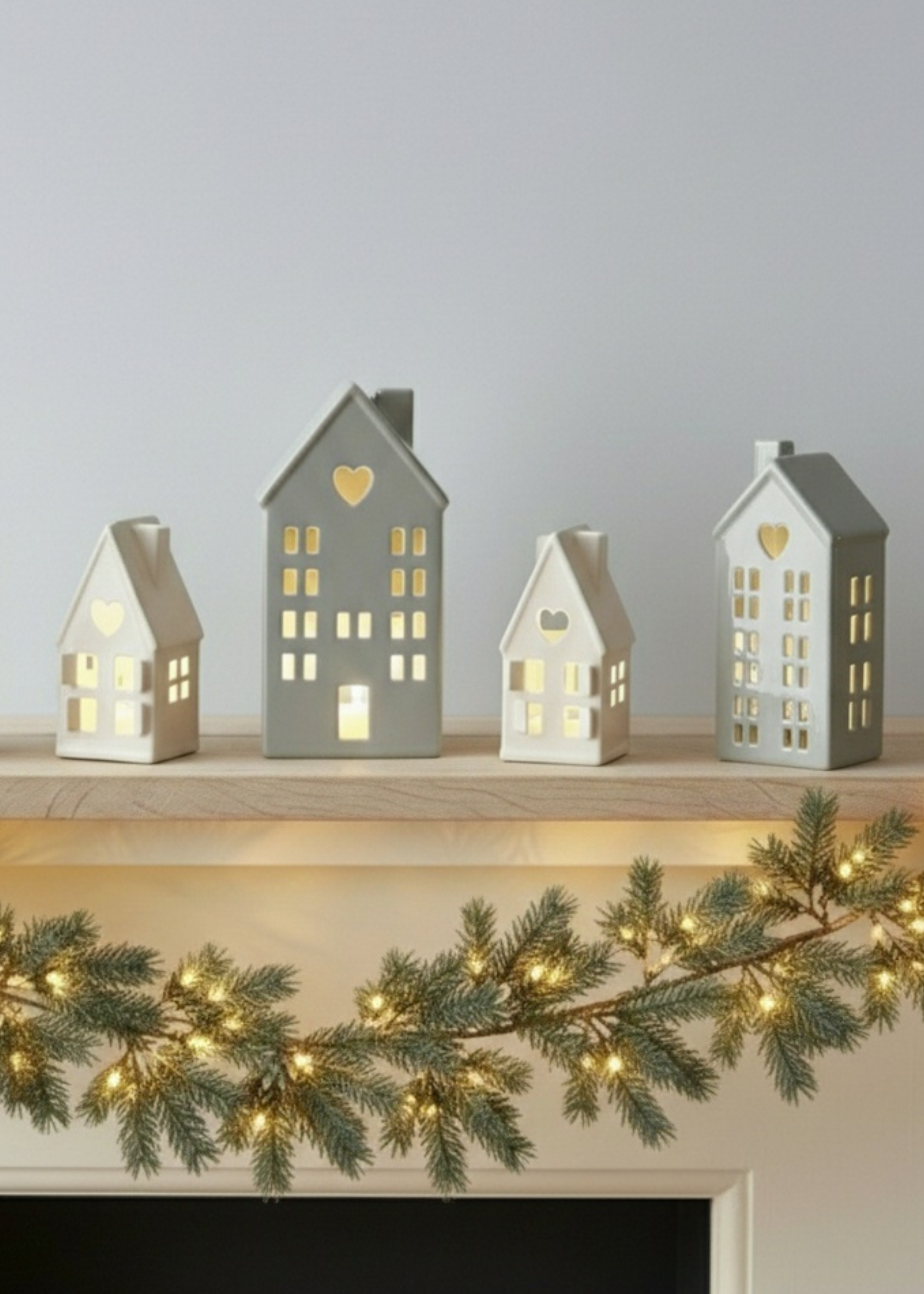 Truly Lifestyle Set of small house-shaped lanterns on a mantelpiece with a Christmas garland.