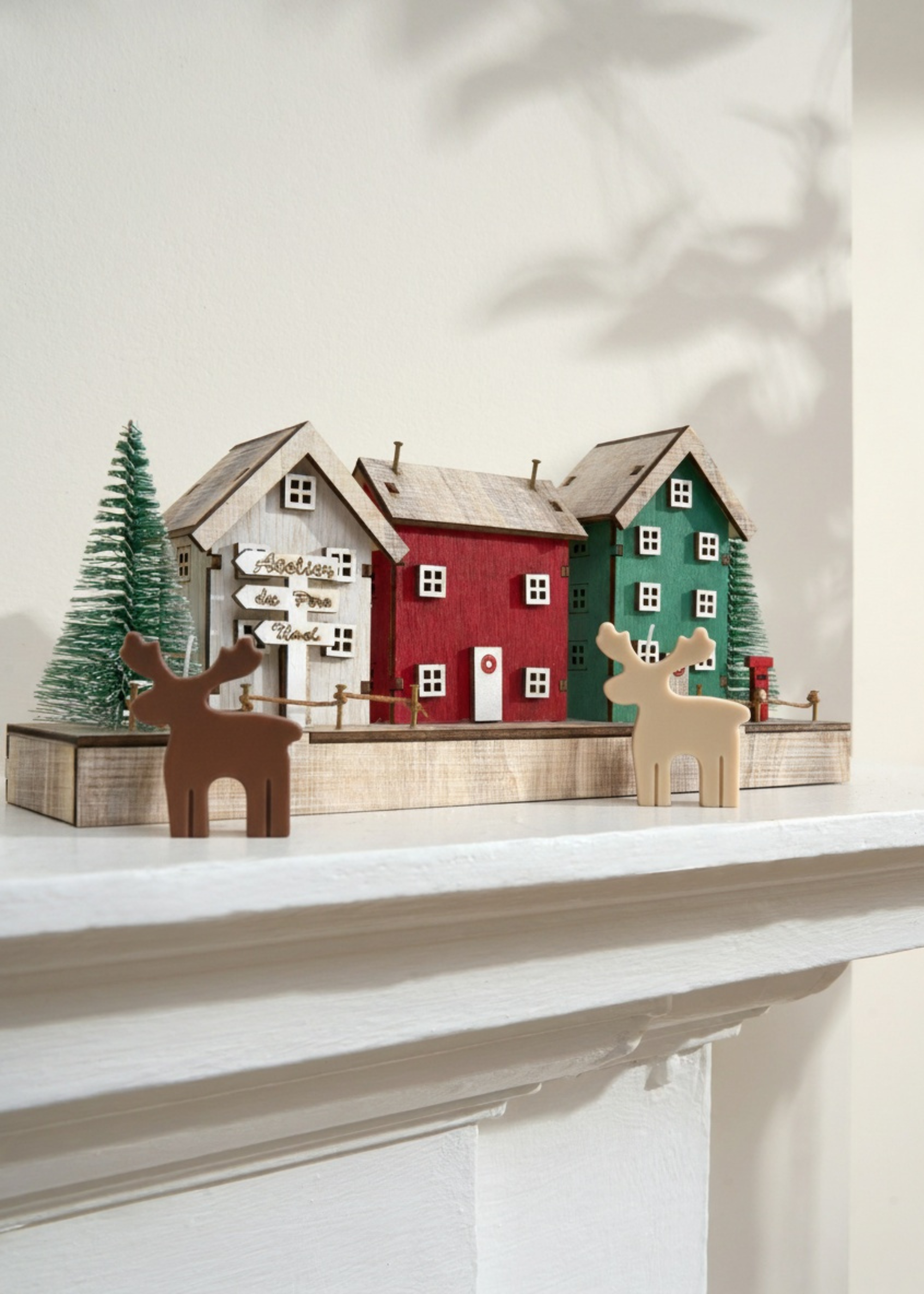 Truly Lifestyle Decorative scene with houses, trees, and reindeer candles on a shelf.
