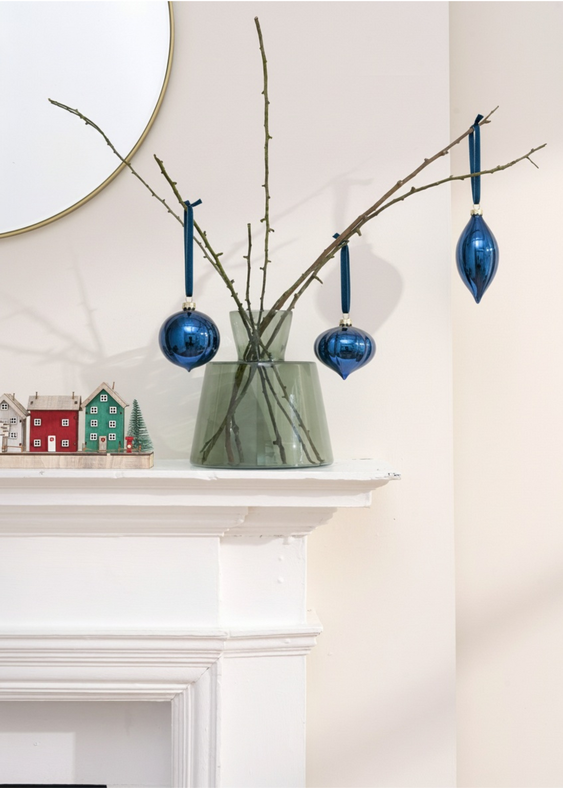 TRULY LIFESTYLE Decorative branch with blue ornaments on a white fireplace mantle.