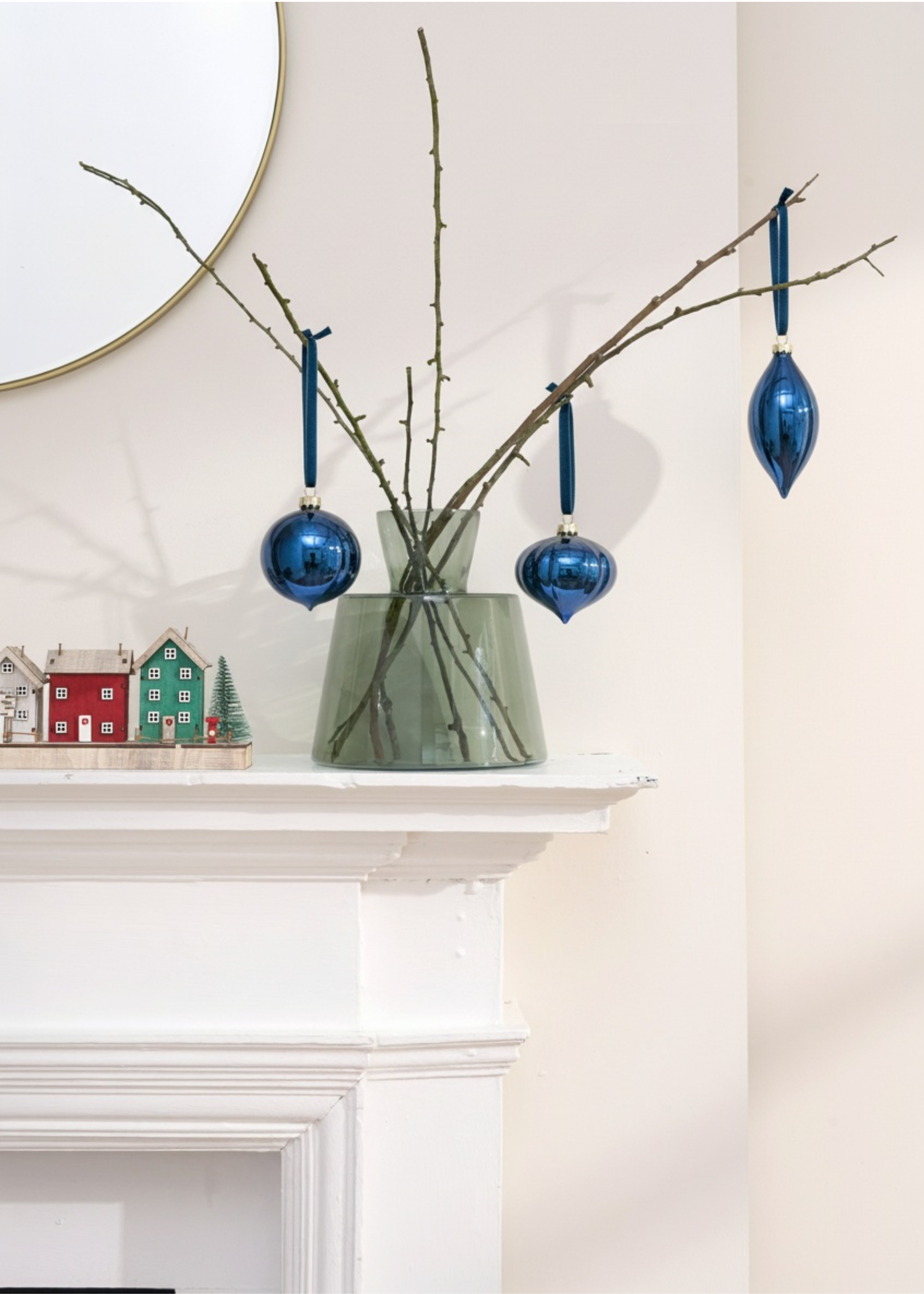 TRULY LIFESTYLE Decorative branch with blue ornaments on a white fireplace mantle.