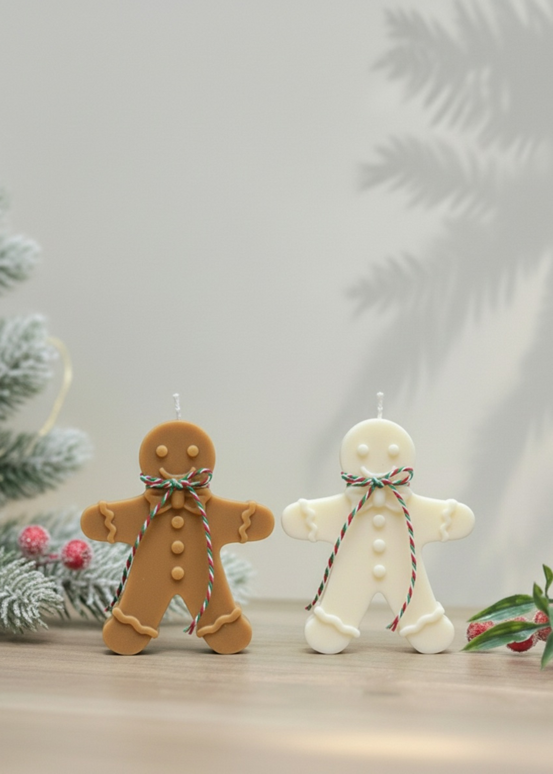 Truly Lifestyle Two gingerbread-themed candles on a wooden surface with a Christmas tree in the background.