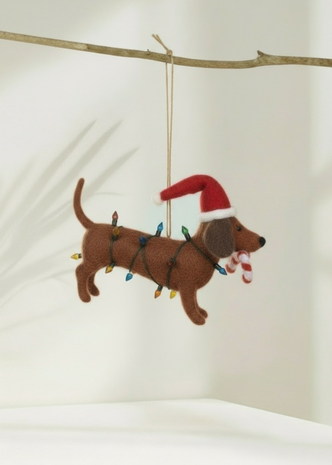 Truly Lifestyle Christmas Felt dachshund ornament with Santa hat and candy cane on a branch against a white background