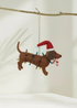 Truly Lifestyle Christmas Felt dachshund ornament with Santa hat and candy cane on a branch against a white background