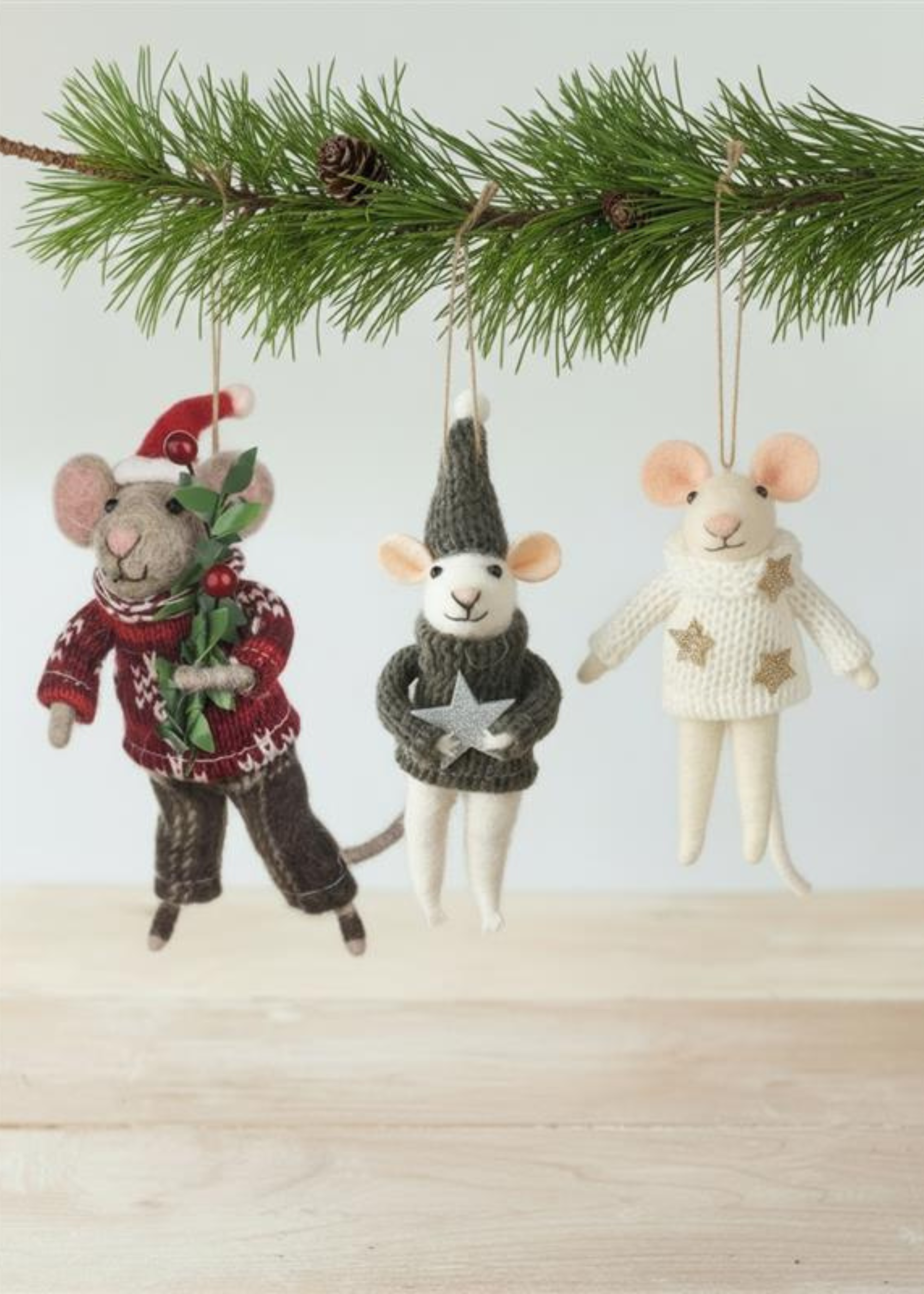 Three knitted mouse ornaments in different outfits hanging from a Christmas tree branch by Truly Lifestyle.