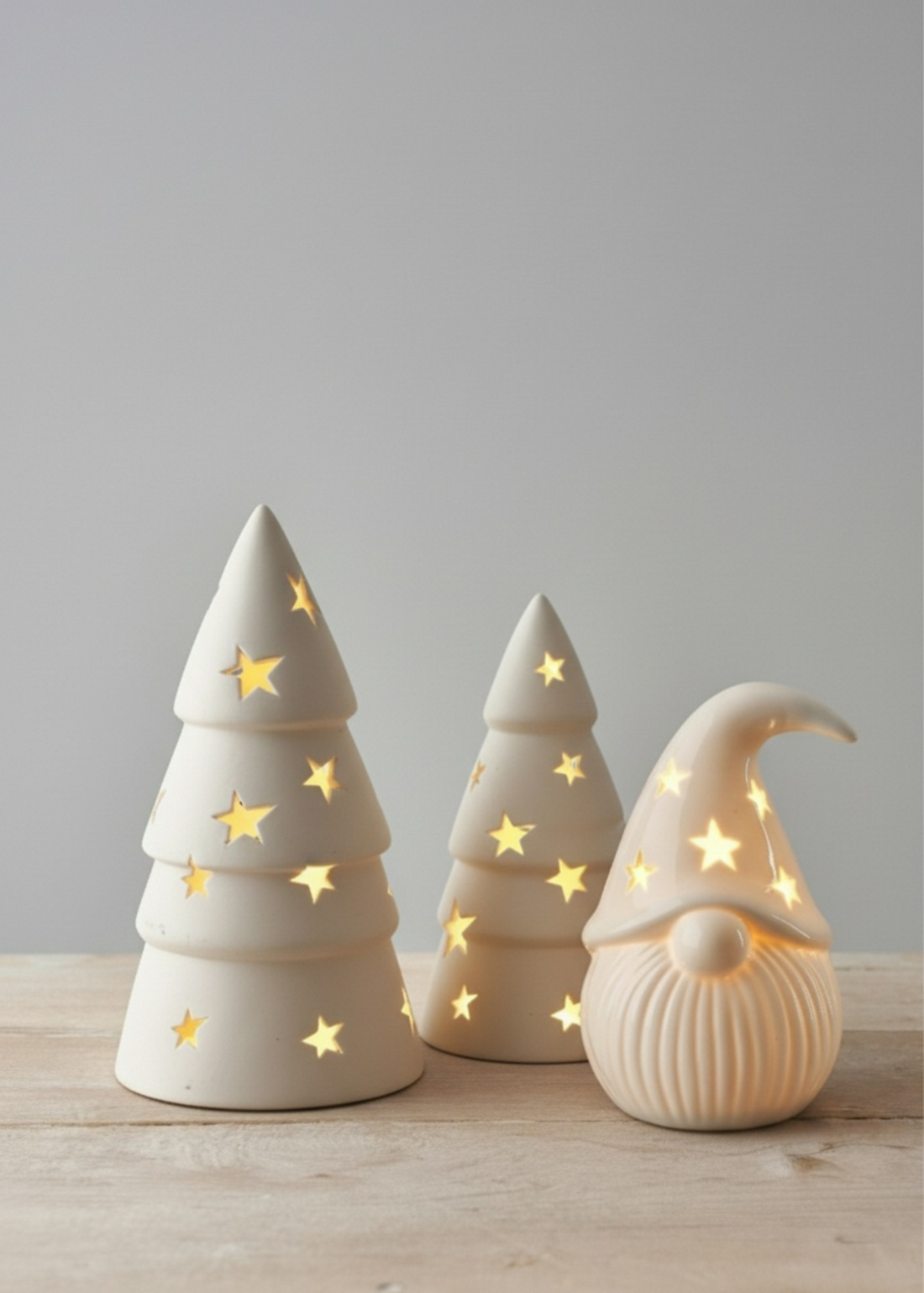 Truly Lifestyle Three ceramic decorative items shaped like a Christmas tree and a gnome with glowing stars on a wooden surface.