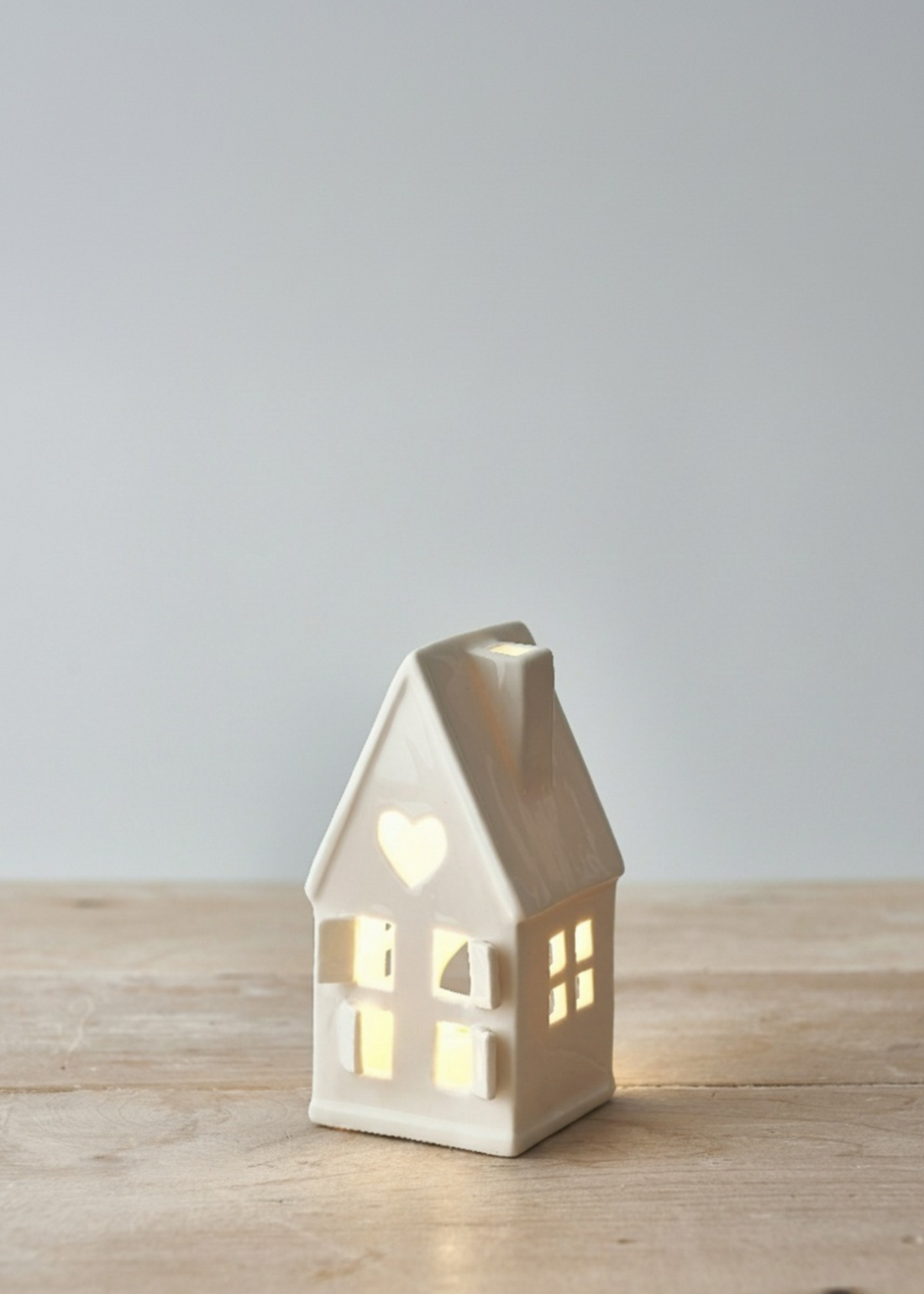 Truly Lifestyle White Ceramic house-shaped lantern with a warm glow on a wooden surface.