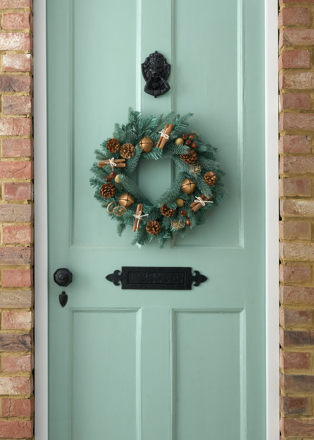 TRULY LIFESTYLE CHRISTMAS WREATH WITH DRIED CINNAMON, ACORNS, ORANGES AND BRONZE BELLS ON GREEN DOOR