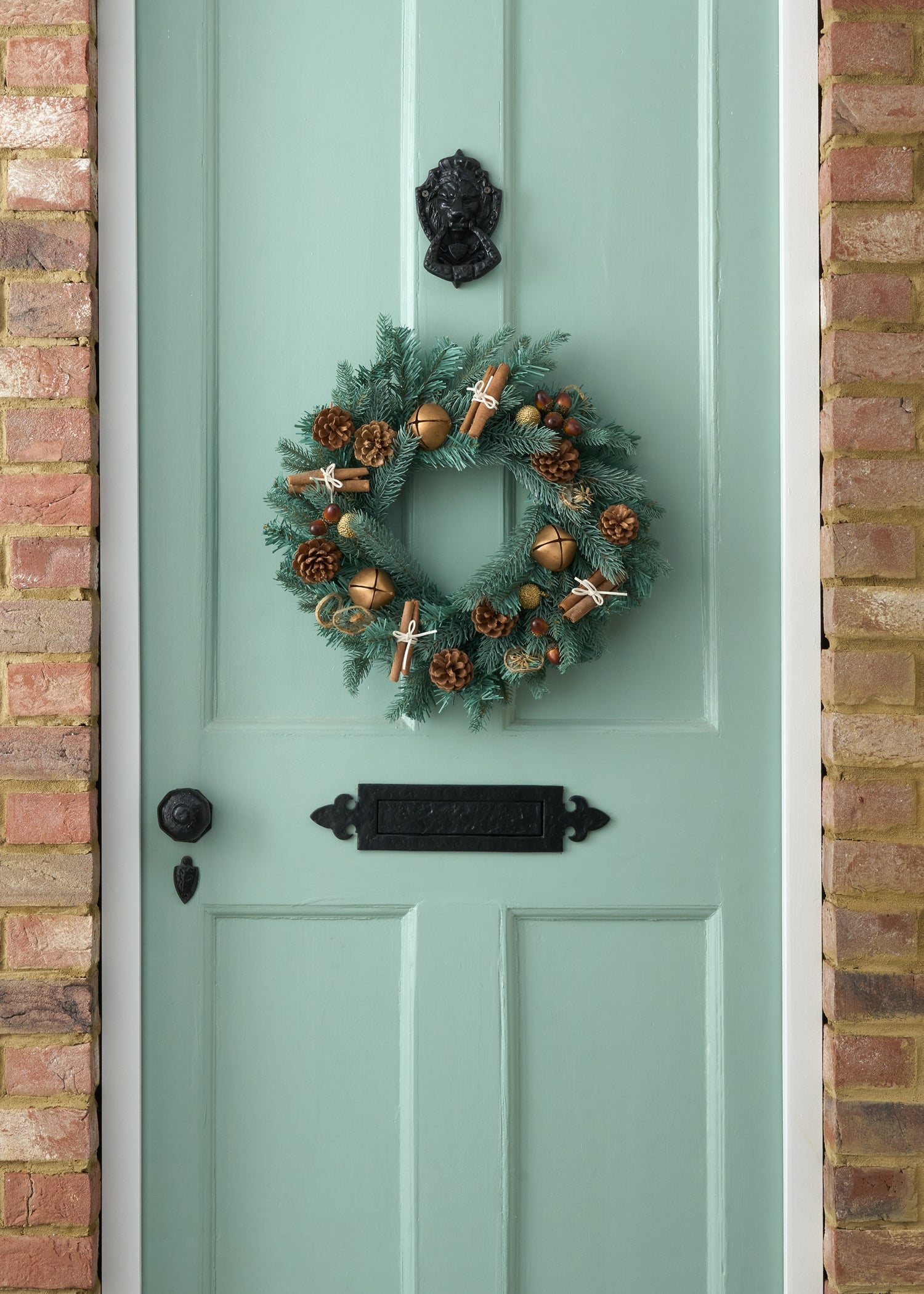 TRULY LIFESTYLE CHRISTMAS WREATH WITH DRIED CINNAMON, ACORNS, ORANGES AND BRONZE BELLS ON GREEN DOOR
