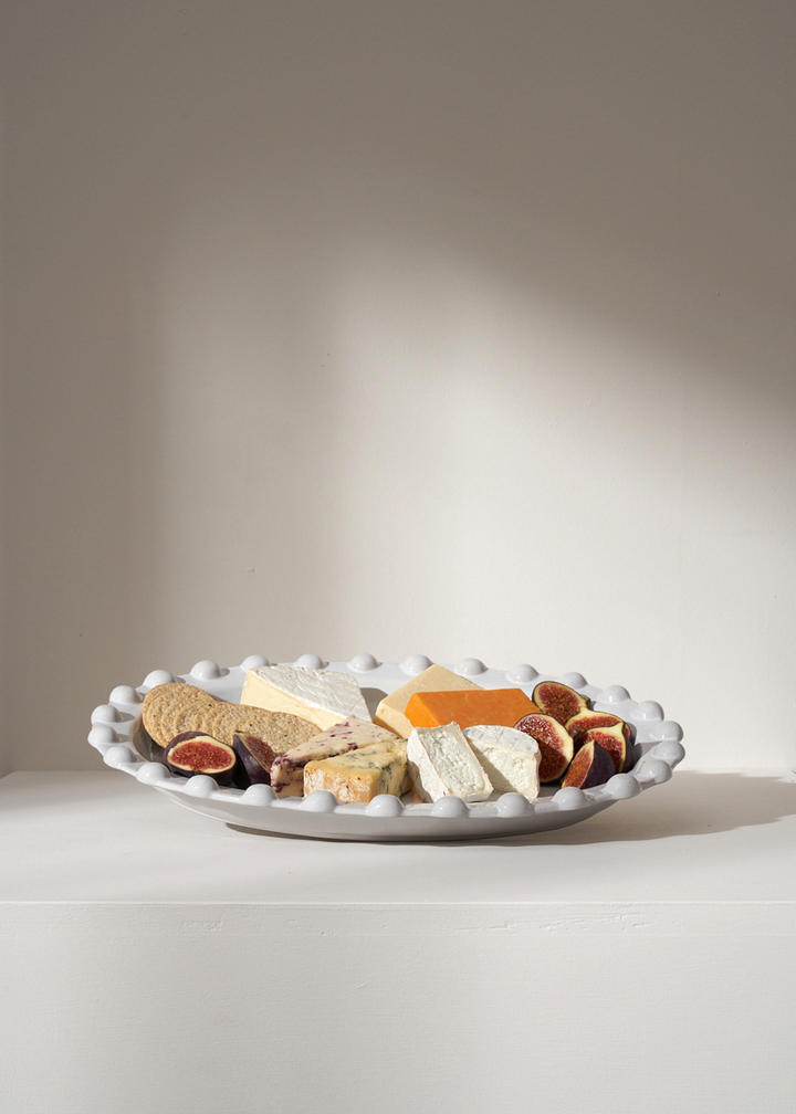 TRULY LIFESTYLE PALE GREY OVAL POM POM EDGED SERVING PLATTER WITH CHEESE, FIGS AND CRACKERS ON IT